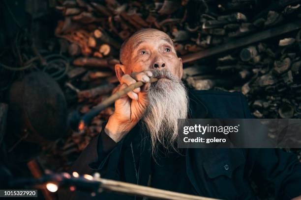 pensive old chinese senior man smoking pipe - wise stock pictures, royalty-free photos & images