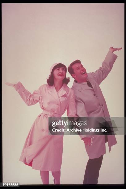 couple in raincoat with hands up, 1962 - vintage rainwear stockfoto's en -beelden