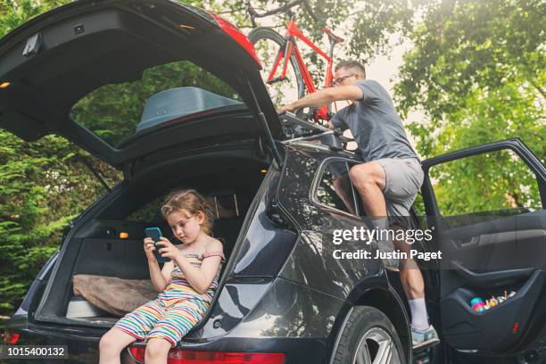 man loading bike onto roofrack - roadtrip preparation - family holiday europe stockfoto's en -beelden