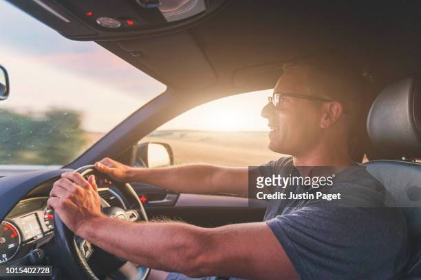 man driving car at sunset - driving photos et images de collection