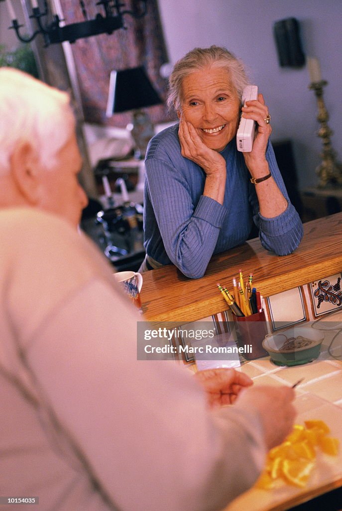 Mature couple in kitchen, woman talking on remote phone