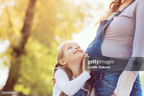little child girl listening to her mothers belly on a sunny day outdoors - little kids belly imagens e fotografias de stock
