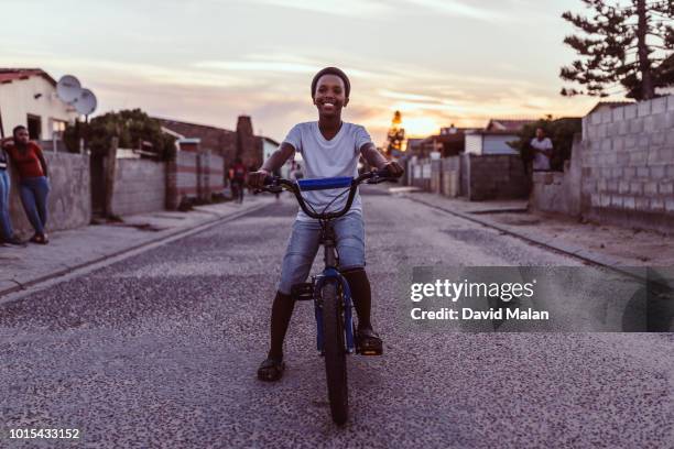 boy on his bicycle in a suburban street at sunset. - township - fotografias e filmes do acervo