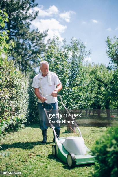 senior man mowing the lawn in his garden - mowed lawn stock pictures, royalty-free photos & images