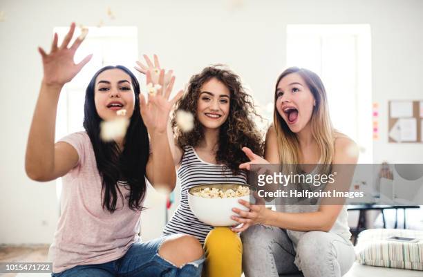three female teenager friends eating popcorn at home, having fun. - throwing phone stock pictures, royalty-free photos & images