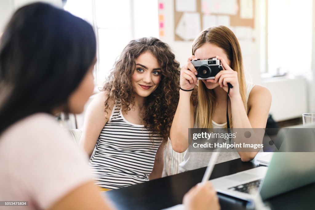 Three female teenager friends with digital camera indoors, taking photo of each other.