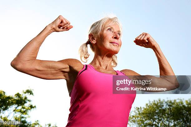 older woman flexes muscles.  - bicep stock-fotos und bilder