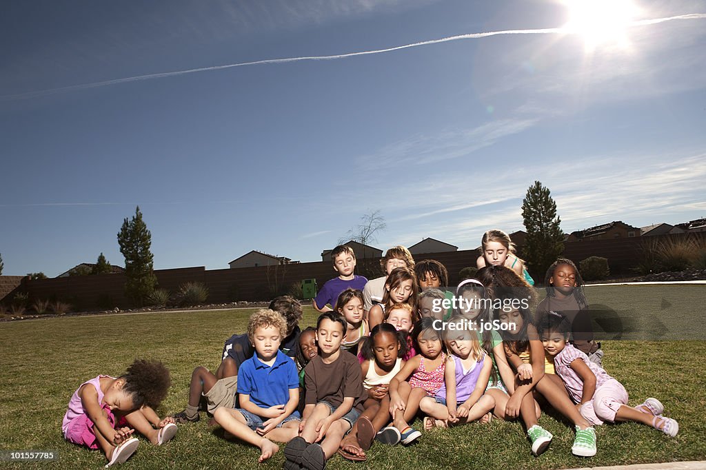 Kids sitting together on grass, tired, eyes closed