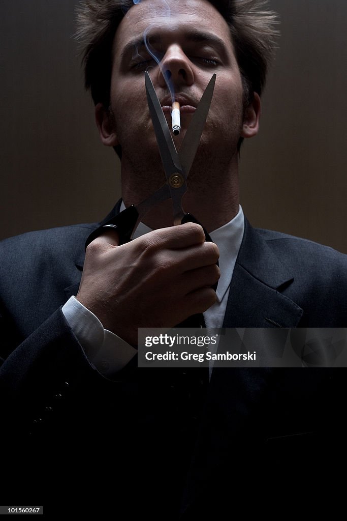 Young man in suit cutting cigarette with scissors