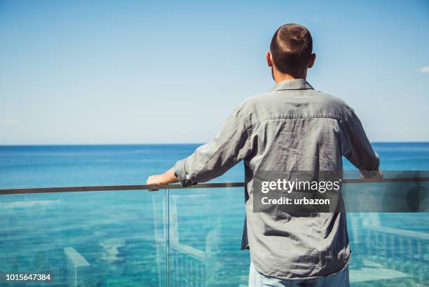man enjoys seaside viewpoint from balcony - beach balcony stock pictures, royalty-free photos & images