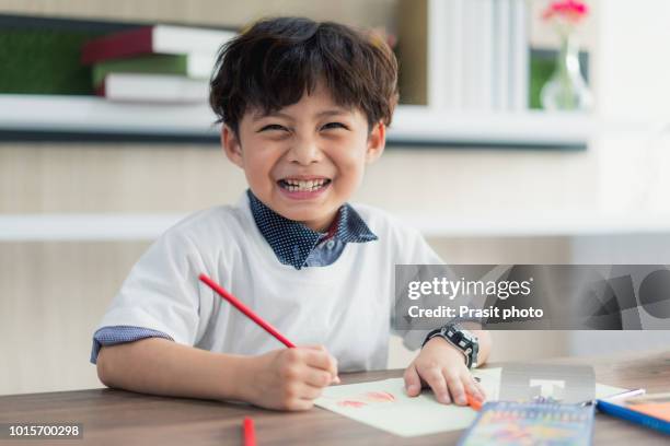 cute little school boy drawing with color pencilsand looking at camera at classroom in school. - boy thailand stock-fotos und bilder