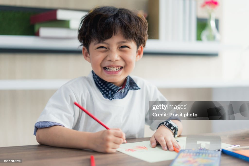Cute little school boy drawing with color pencilsand looking at camera at classroom in school.