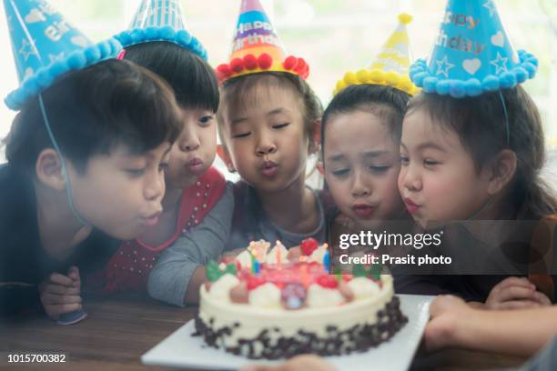 asian child on birthday party blowing candles on cake being helped by friends. group of adorable kids having fun at birthday party. - parents children blow candles asians foto e immagini stock