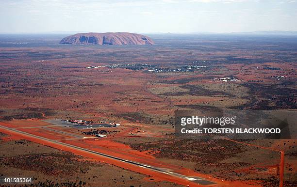 The resort town of Yulara and Connellan Airport lie before the arkose massif of Uluru rising 348 metres above the surrounding desert of central...