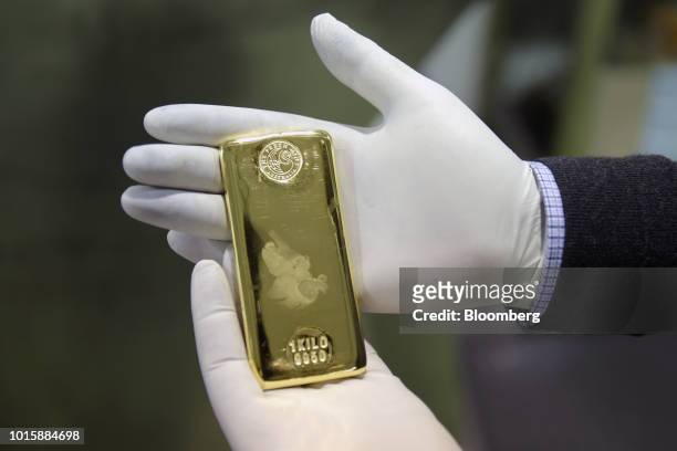 An employee holds a one kilogram gold bar for a photograph at the Perth Mint Refinery, operated by Gold Corp., in Perth, Australia, on Thursday, Aug....