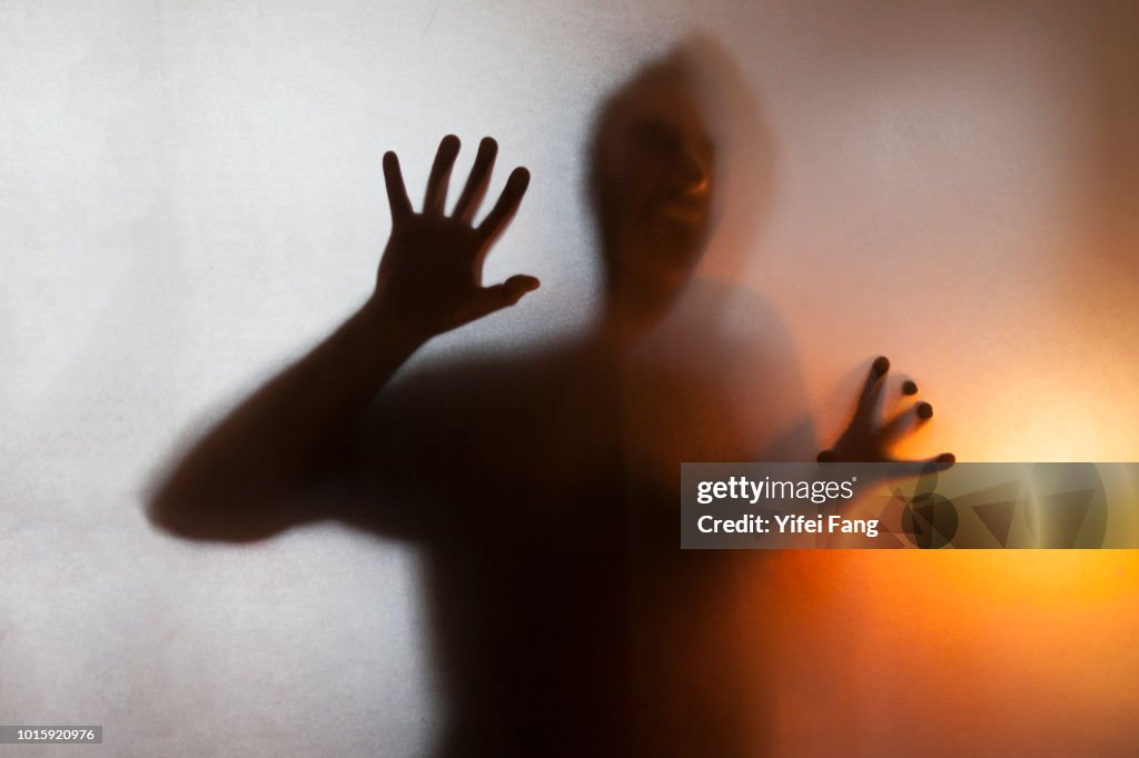 Man with hands pressed up against glass behind translucent facade