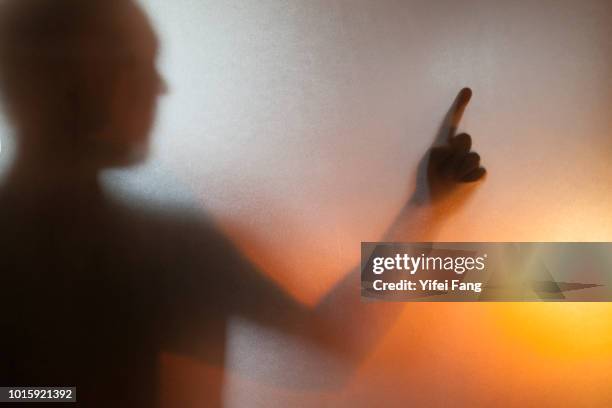 silhouette of arm and hand with one finger pointing behind translucent glass - hands behind glass stock pictures, royalty-free photos & images