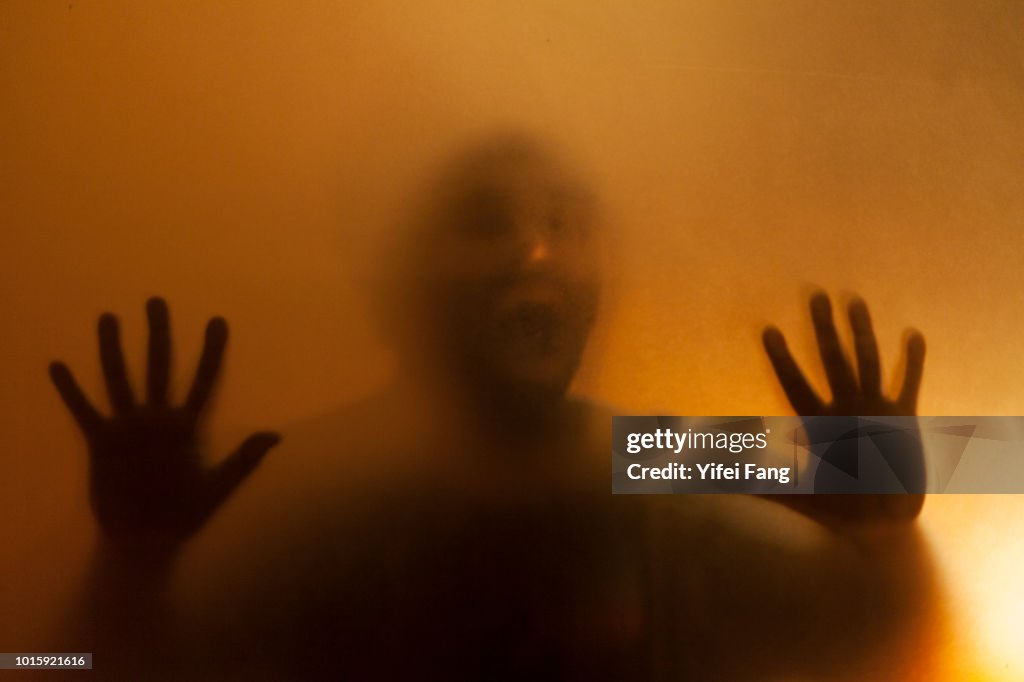 Man with hands pressed up against glass behind translucent facade