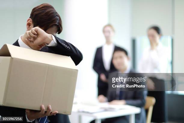 businessman carrying box of belongings,colleagues in background - despedido fotografías e imágenes de stock