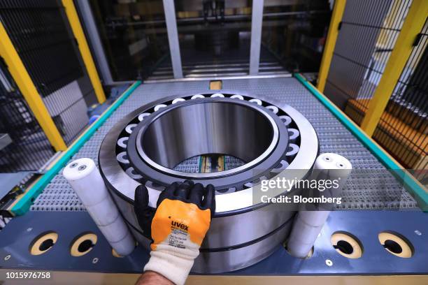 An employee places a steel roller bearing into a protective coating machine on the assembly line inside the Schaeffler AG factory in Schweinfurt,...