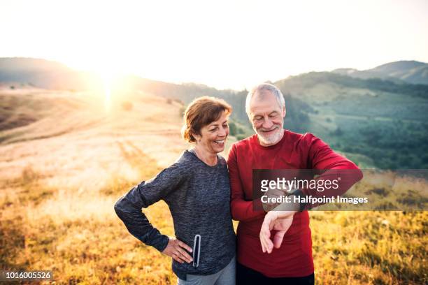 senior couple runners resting outdoors in nature at sunrise, using smart watch. - computador utilizável como acessório imagens e fotografias de stock