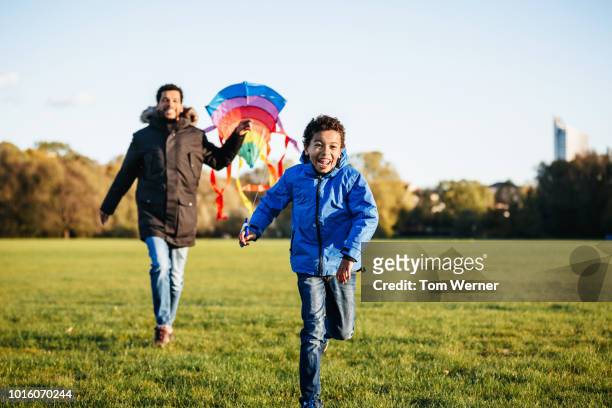 single dad running with son in park - blue coat stock pictures, royalty-free photos & images