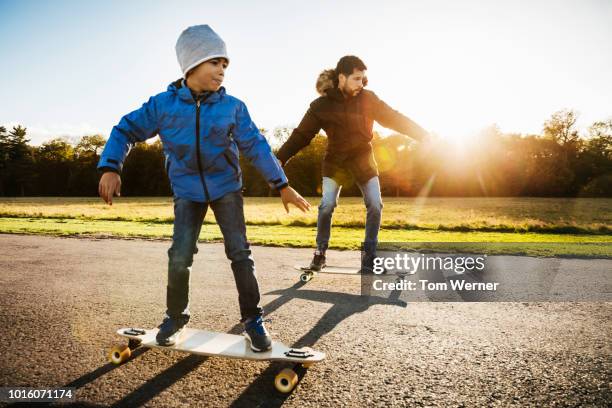 young boy long boarding with his dad - boys sport pants stock pictures, royalty-free photos & images