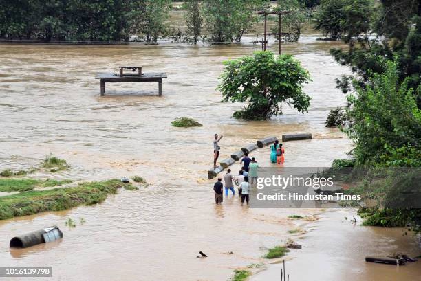 People make their way through flooded Suketi Khad river after heavy rainfall in Balh valley on August 13, 2018 in Mandi, India.