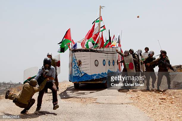 An Israeli soldier tries to arrest a journalist as Palestinian protesters use a replica of the Gaza aid flotilla near an Israeli barrier, as they...