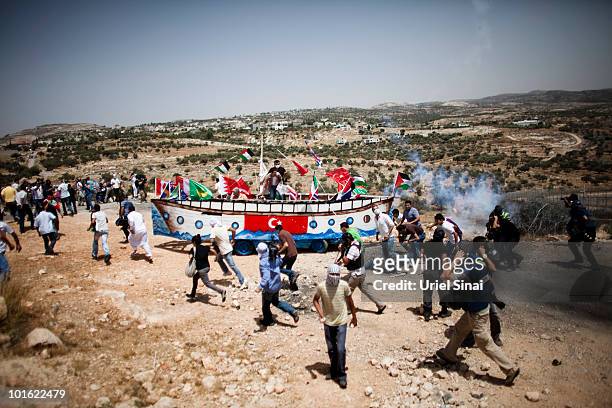 Palestinian protesters run from tear gas as they use a replica of thje Gaza aid flotilla vessel near an Israeli barrier, as they object to Israel's...