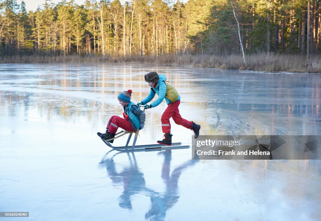 Boy pushing his brother on sleigh across frozen lake