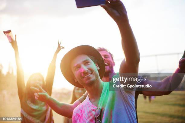 four young adult friends covered in coloured chalk powder taking selfie at holi festival - music festival day 4 stockfoto's en -beelden