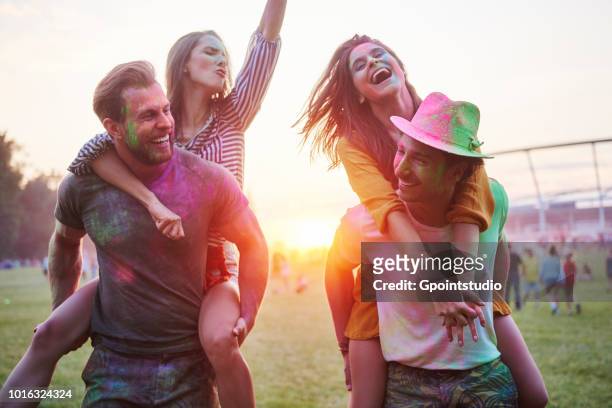 two young couples covered in coloured chalk powder piggybacking at holi festival - farbpulver stock-fotos und bilder