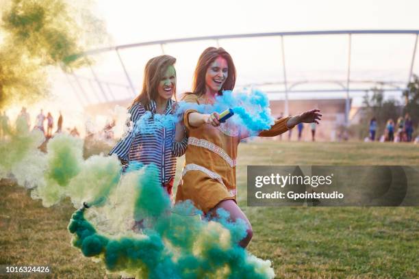 two young women dancing with coloured smoke bombs at holi festival - katowice stock pictures, royalty-free photos & images