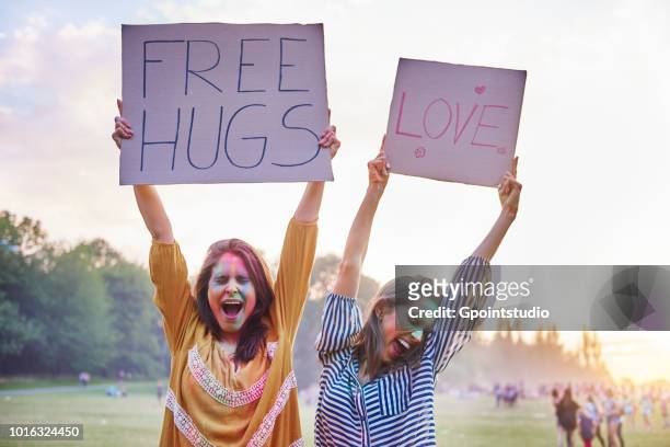 young women dancing holding up love and free hug signs at holi festival - free sign stock pictures, royalty-free photos & images