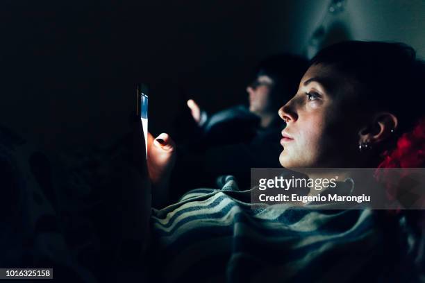 women in bed in darkness using mobile phones - couple smartphone stockfoto's en -beelden