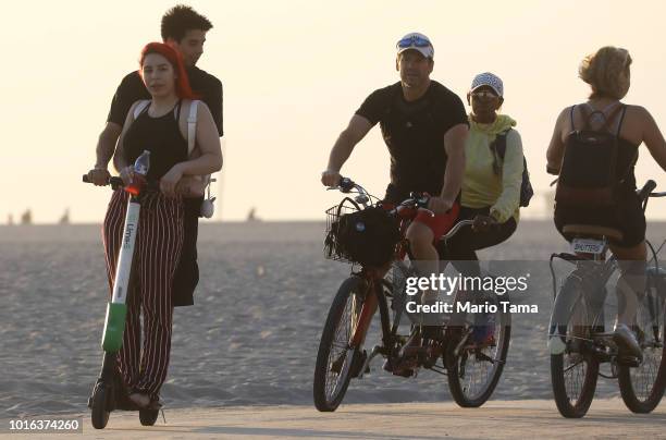 Man and woman ride a shared dockless electric scooter next to bicycles along Venice Beach on August 13, 2018 in Los Angeles, California. Shared...