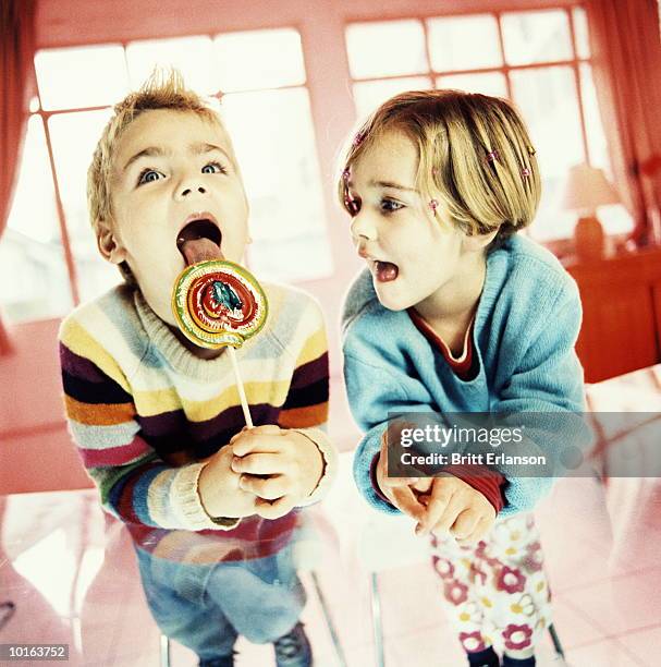 boy licks lollypop, girl watches - neid stock-fotos und bilder