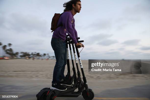 Man rides a Bird shared dockless electric scooter while transporting three others along Venice Beach on August 13, 2018 in Los Angeles, California....