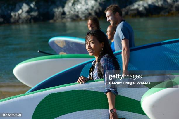 asian woman smiling as part of a group carrying sup paddle boards. - paddleboarding team stock pictures, royalty-free photos & images