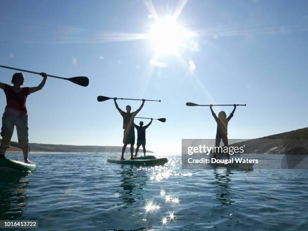 Group of friends SUP paddle boarding at sea raising paddles above head.