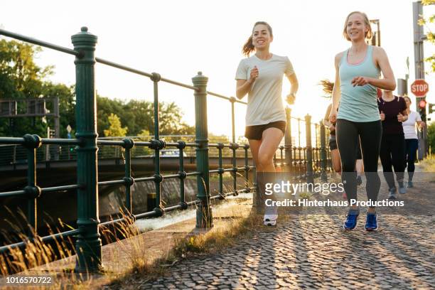 group of women running together alongside canal - jogging stock-fotos und bilder
