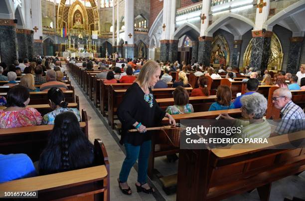 Volunteer collects the tithe during a mass at La Coromoto Church, in Caracas on August 12, 2018. - The shortage of cash in the country has forced...