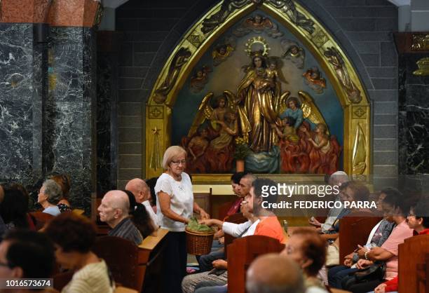Catholic faithful give alms to volunteers during a mass at La Coromoto Church, in Caracas on August 12, 2018. - The shortage of cash in the country...