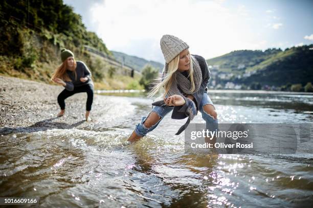 two female friends skipping stones on a river - natural blonde stock-fotos und bilder