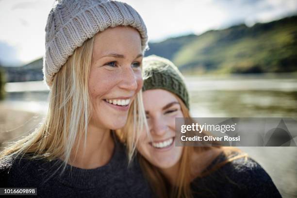 portrait of two smiling female friends wearing knit hats at the riverbank - woolly hat - fotografias e filmes do acervo