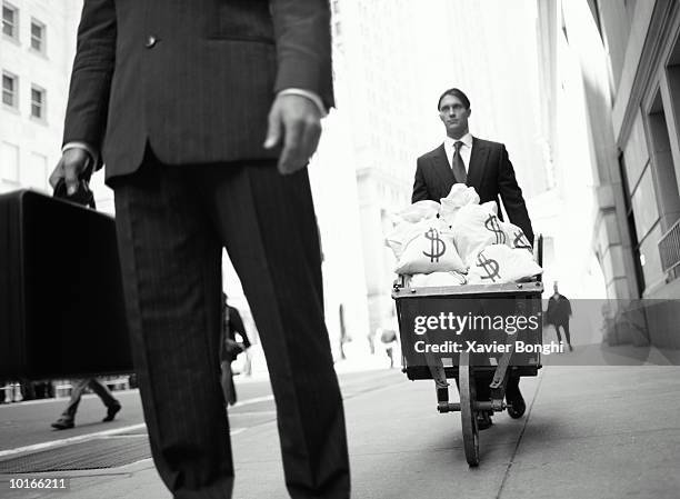 businessman with wheelbarrow of money - avarice fotografías e imágenes de stock