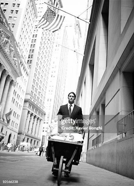 businessman with wheelbarrow full of money - young-urban-professional-person stock-fotos und bilder