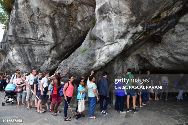 Catholic pilgrims touch the rock inside the Massabielle Cave where the Virgin Mary is said to have appeared to Bernadette Soubirous, during the Feast...