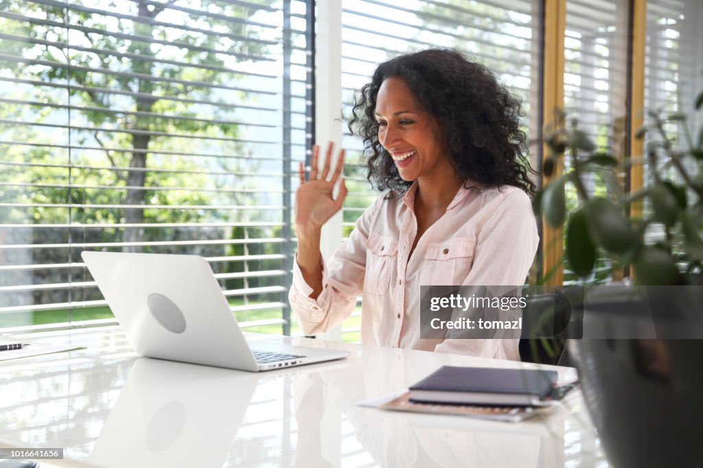 Woman waving at laptop in the middle of a video conference call